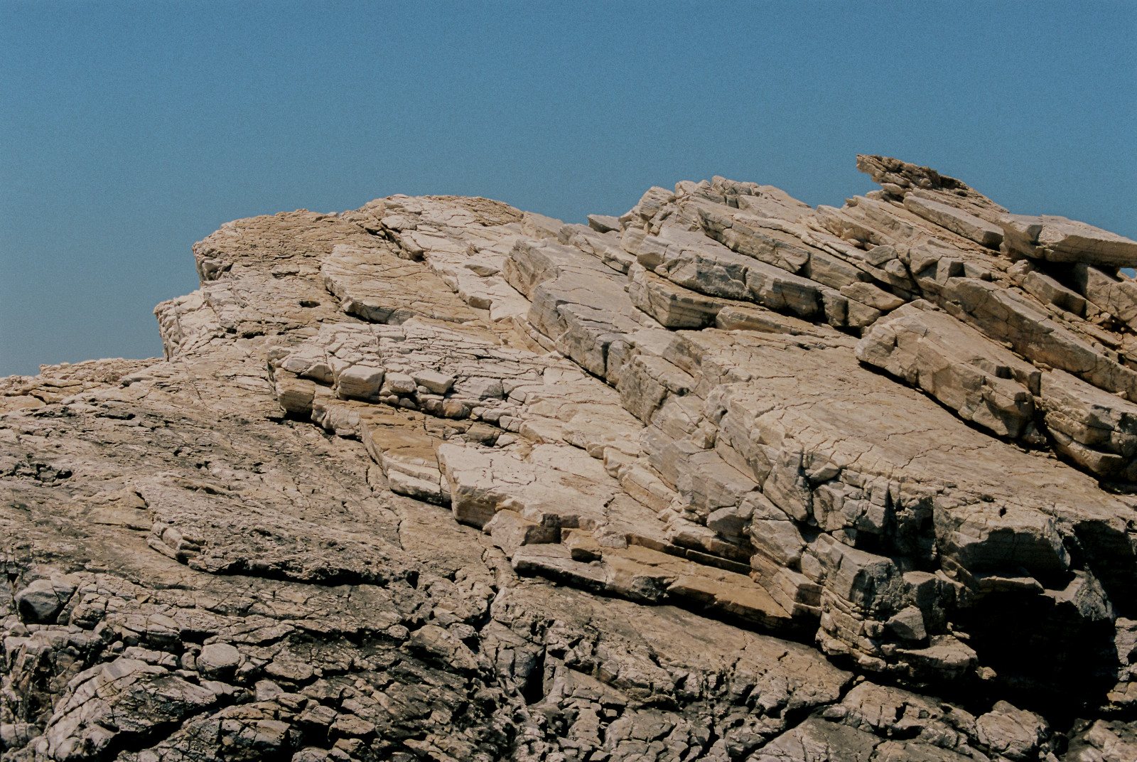 Pale stone rises in thin, cracked layers against a clear blue sky.