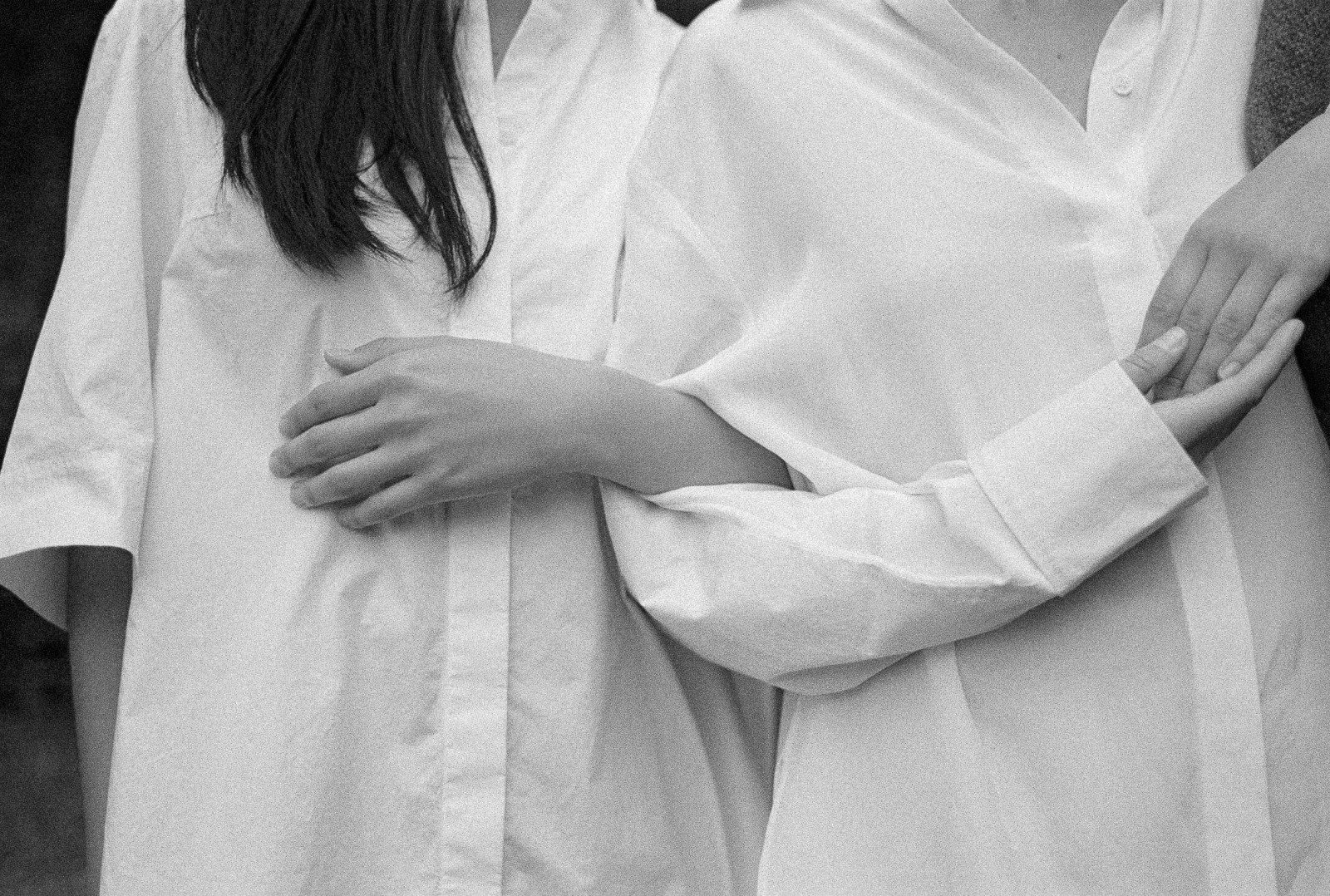 Two people in white shirts stand side by side with their arms linked, in black and white.