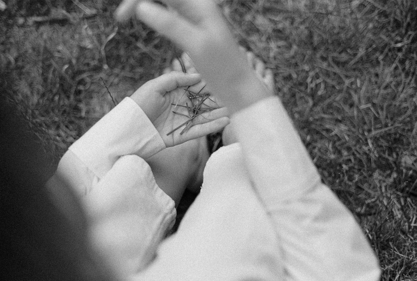 A person in a white shirt holds a few pine needles in an open palm, in black and white.