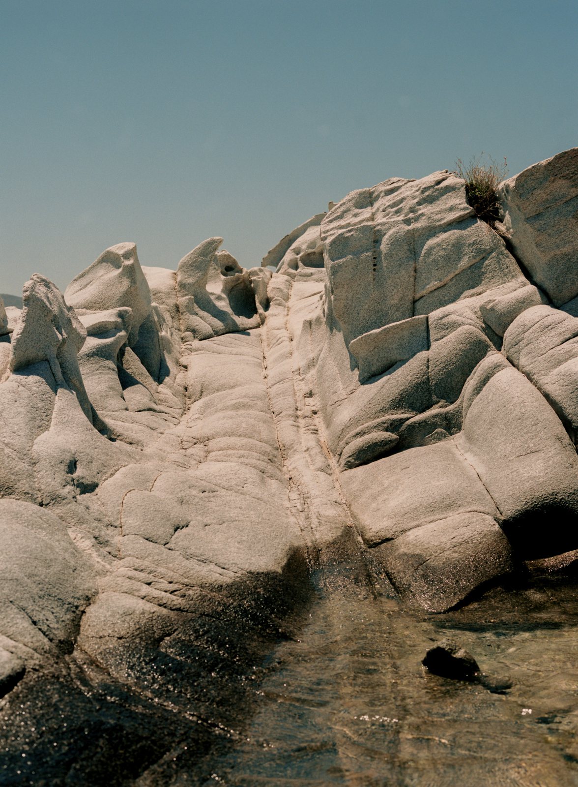 Smooth white granite rises in rounded folds above a pool of clear water.